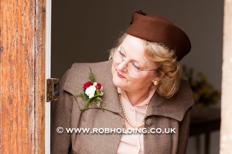 Older woman in a beige outfit and hat standing by a wooden door