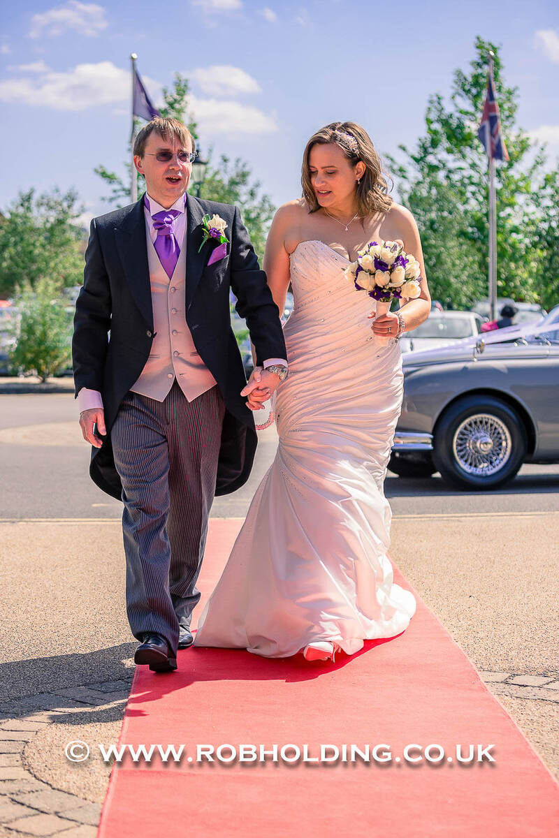 Groom and bride walking together along a red carpet outdoors