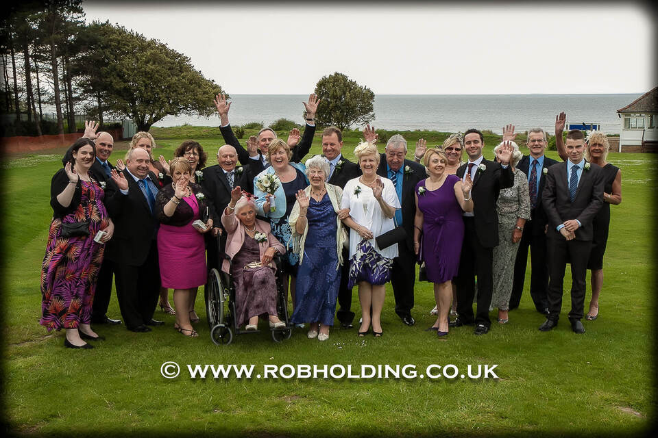 Large group photo of wedding guests on a coastal lawn