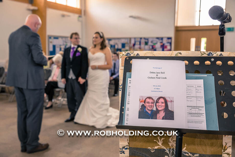 Wedding guests at the ceremony beside an order of service stand