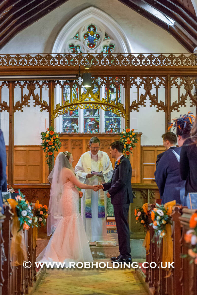 Bride and groom holding hands at the altar with the priest
