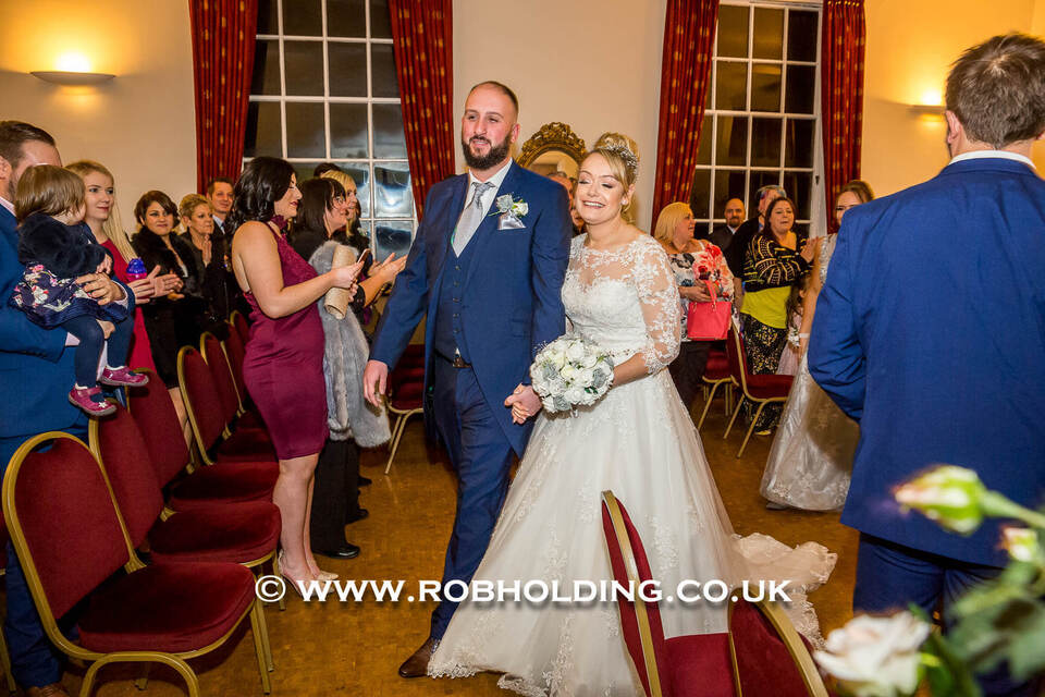 Bride and groom walking down the aisle indoors as guests clap