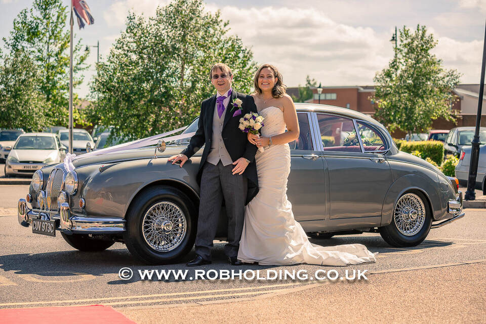 Bride and groom standing beside a vintage car outdoors